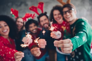 Happy employees holding sparklers and wearing festive hats at office holiday party