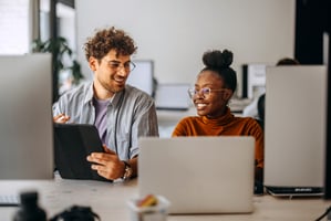 Two smiling interns conversing at their computers