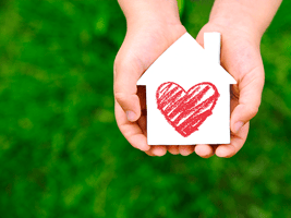 Hands holding a house cut-out with a heart drawn in the center.