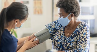 Female doctor taking blood pressure of older women wearing a mask 